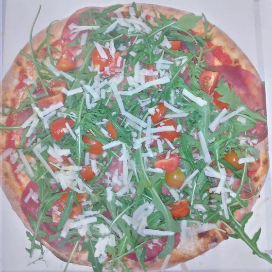 Una pizza con rucola, pomodorini e grana nel cartone d'asporto